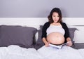 Pregnant woman reading a book while lying on a bed in the bedroo Royalty Free Stock Photo