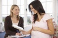 Pregnant Woman Reading Information Booklet At Home With Health Visitor