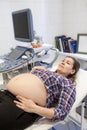 Pregnant woman ready for ultrasound and screening procedures. Medical equipment, scanner and monitor are in inspection room