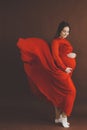 Pregnant woman in red flying dress holding her belly Royalty Free Stock Photo