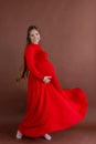 Pregnant woman in red flying dress holding her belly Royalty Free Stock Photo