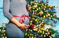 Pregnant woman with red ribbon near New Year tree