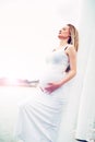 Pregnant woman relaxing against a white pillar