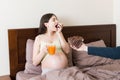 Pregnant woman relaxing in bed is eating chocolate cereal balls and drinking juice. Husband is feeding his wife. Dry breakfast Royalty Free Stock Photo