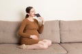 Pregnant woman relaxing on the sofa is eating a bar of chocolate at home. Unhealthy food during pregnancy concept Royalty Free Stock Photo