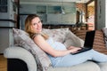 Pregnant woman resting on sofa and working on laptop.