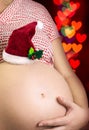 Pregnant woman's cute belly with Santas hat and hearts bokeh Royalty Free Stock Photo