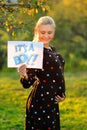 Pregnant woman on second trimester posing in sunny garden, shows a slogan its a boy