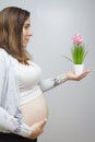 Pregnant woman showing belly in light colors holding a plant wit