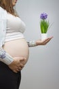 Pregnant woman showing belly in light colors holding a plant wit
