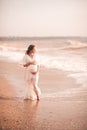 Pregnant woman showing heart shape with fingers wearing white dress over sea background. Motherhood. Maternity. Royalty Free Stock Photo