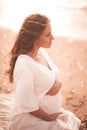 Pregnant woman showing heart shape with fingers wearing white dress over sea background. Motherhood. Maternity. Royalty Free Stock Photo