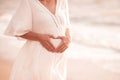 Pregnant woman showing heart shape with fingers wearing white dress over sea background. Motherhood. Maternity. Royalty Free Stock Photo