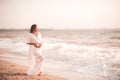 Pregnant woman showing heart shape with fingers wearing white dress over sea background. Motherhood. Maternity. Royalty Free Stock Photo