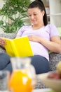 Pregnant woman siting on a sofa and reading a book