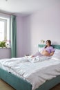 A pregnant woman sits in bed of her domestic bedroom and looking oout the window. Female enjoying her pregnancy state Royalty Free Stock Photo