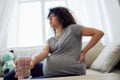 A pregnant woman sits on the couch with lower back pain and headache, strain on the spine during pregnancy drinks water