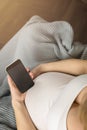 A pregnant woman sits covered with a blanket and holds a phone in her hands. Royalty Free Stock Photo