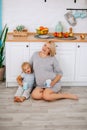 A pregnant woman sits with a little blonde girl on the floor in the kitchen with cups in her hands Royalty Free Stock Photo