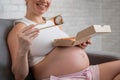 A pregnant woman sits on the sofa and eats rolls from a box. Food delivery.