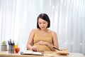 A pregnant woman sits at a table and uses a tablet computer