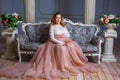 A pregnant woman sitting in a beautiful dress on the couch. the concept of motherhood
