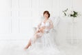 Pregnant woman sitting in a chair in a beautiful white dress boudoir . Royalty Free Stock Photo
