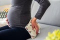 Pregnant woman sitting comfortably on the sofa and holding a therapeutic heat pillow on her lower back Royalty Free Stock Photo