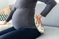 Pregnant woman sitting comfortably on the sofa and holding a therapeutic heat pillow on her lower back Royalty Free Stock Photo