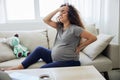 Pregnant woman sitting on the couch lower back pain and headache, strain on the spine during pregnancy. Lifestyle