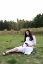 Pregnant woman sitting on grass lawn enjoy peaceful sunset sunrise in nature Asian Chinese outdoor expecting baby earphone belly Royalty Free Stock Photo