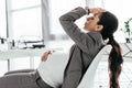 Pregnant woman sitting in office in chair near table and holding hear with hand Royalty Free Stock Photo