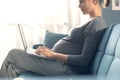 Pregnant woman sitting on the sofa and connecting with her laptop Royalty Free Stock Photo