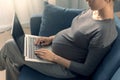Pregnant woman sitting on the sofa and connecting with her laptop Royalty Free Stock Photo