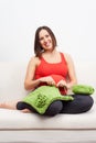 Pregnant woman sitting on sofa and crocheting