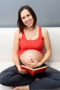 Pregnant woman sitting on sofa and holding book Royalty Free Stock Photo