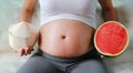 Pregnant woman sitting on sofa with holding coconut and cut half watermelon at her belly Royalty Free Stock Photo