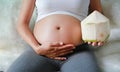 Pregnant woman sitting on sofa and holding coconut at her belly Royalty Free Stock Photo