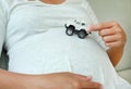 Pregnant woman sitting on sofa playing model of four wheel car on her belly Royalty Free Stock Photo
