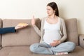 Pregnant woman sitting on the sofa refuses delicious slices of cakes and makes stop gesture. Diet during pregnancy concept