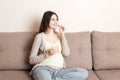 Pregnant woman is sitting in sofa. Taking pills from colds. Last months of pregnancy Royalty Free Stock Photo