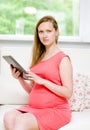 Pregnant woman sitting on sofa and using electronic tablet Royalty Free Stock Photo