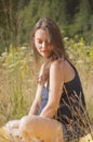 Pregnant woman sitting in the tall grass. The sun shines. Against the background of the forest. The concept of a healthy lifestyle