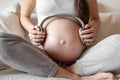 Pregnant woman sitting on white sofa and keeping headphones on belly