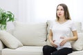 Pregnant woman sitting on white sofa touching her stomach. Royalty Free Stock Photo