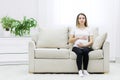 Pregnant woman sitting on white sofa and touching her stomach. Royalty Free Stock Photo