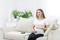Pregnant woman sitting on white sofa and touching her stomach. Royalty Free Stock Photo