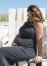 Pregnant woman sitting on wooden chair on the beac Royalty Free Stock Photo