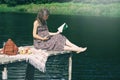 Pregnant woman sitting on wooden pier near lake and reading book. Outdoor picnic near water. Wellbeing and time to relax alone Royalty Free Stock Photo