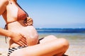 Pregnant woman skin care moisturizer cream on belly on beach at Royalty Free Stock Photo